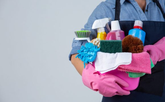 Young girl is holding cleaning product, gloves and rags in the basin on white background
